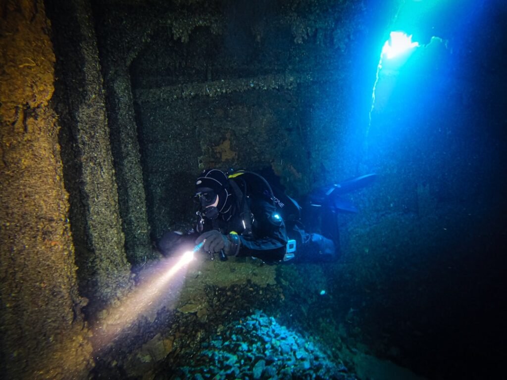 Scuba diver with flashlight exploring dark underwater depths, representing horror survival games like Subnautica