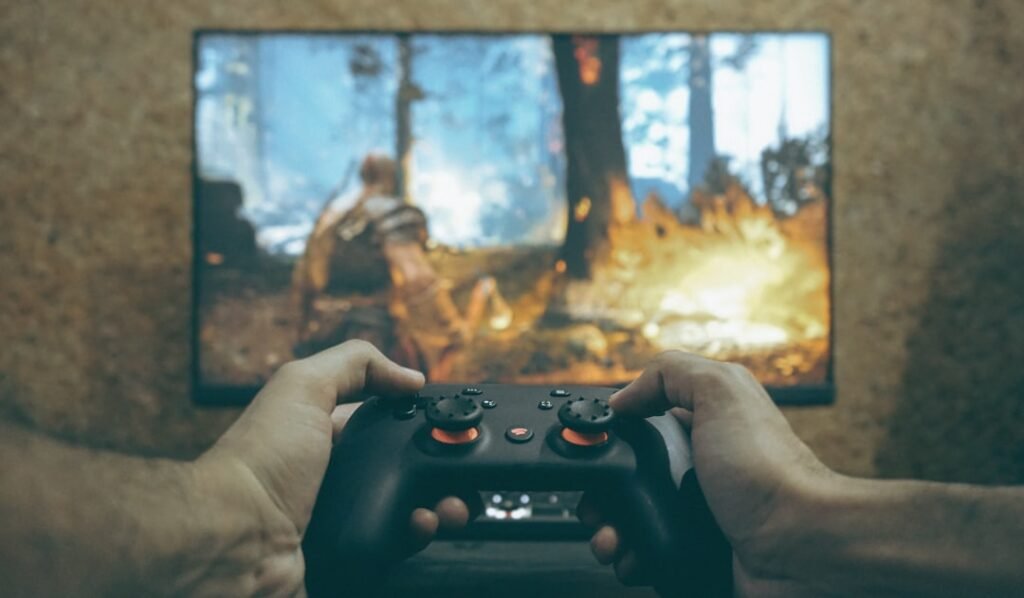 Hands holding a gaming controller with an action game playing on TV screen in background